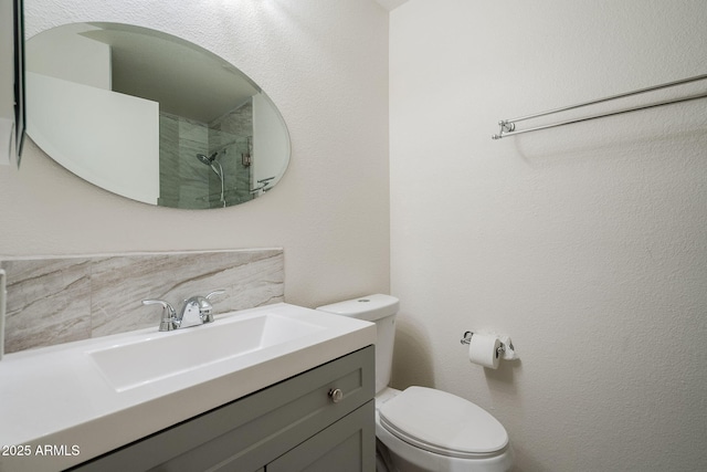 bathroom featuring toilet, vanity, decorative backsplash, and a tile shower