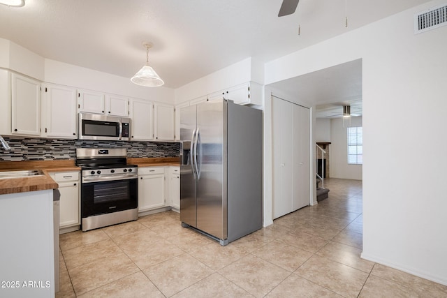 kitchen featuring stainless steel appliances, butcher block counters, white cabinetry, and decorative light fixtures