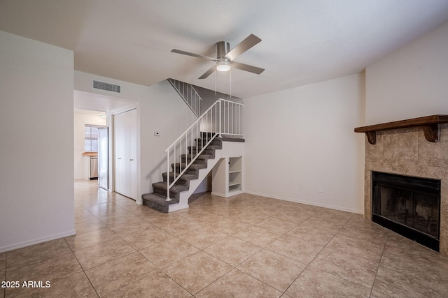 unfurnished living room with ceiling fan, light tile patterned floors, and a tiled fireplace