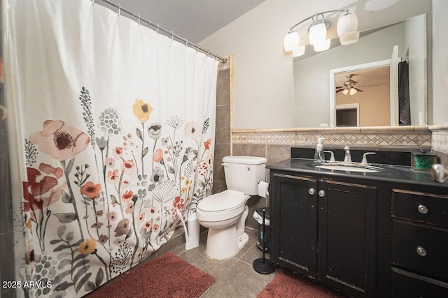 full bathroom with tile walls, vanity, toilet, a ceiling fan, and wainscoting