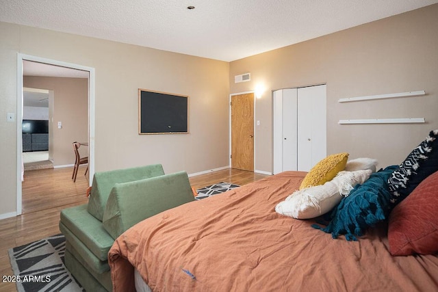bedroom with wood finished floors, baseboards, a closet, and a textured ceiling