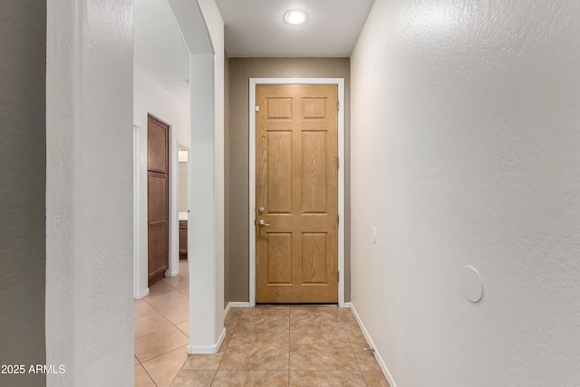 8848 W Cordes Rd, Tolleson, AZ 85353 - corridor featuring light tile patterned floors, a textured wall, baseboards, and arched walkways