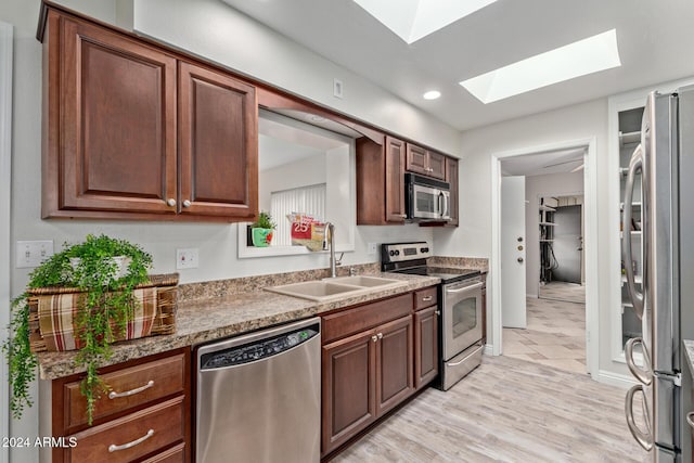 kitchen featuring appliances with stainless steel finishes, light wood-type flooring, a skylight, sink, and dark stone countertops