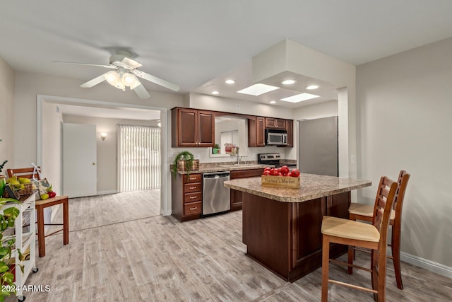 kitchen featuring a kitchen breakfast bar, a skylight, stainless steel appliances, and light wood-type flooring