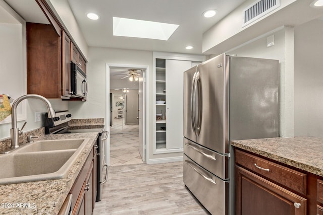 kitchen with a skylight, ceiling fan, sink, stainless steel appliances, and light hardwood / wood-style flooring