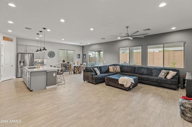 living room with ceiling fan, sink, and light wood-type flooring