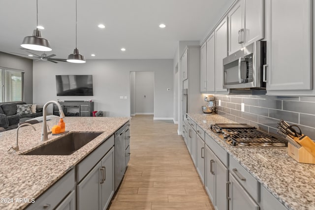 kitchen featuring pendant lighting, sink, ceiling fan, stainless steel appliances, and light stone counters