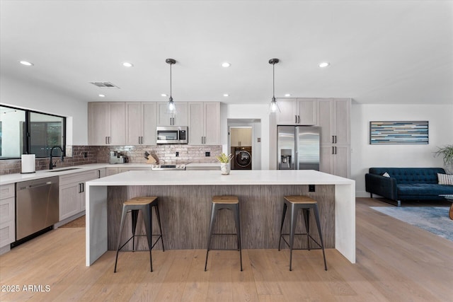 kitchen featuring stainless steel appliances, a kitchen island, decorative light fixtures, and washer / dryer