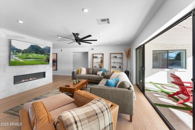 living room with light hardwood / wood-style floors, ceiling fan, and a high end fireplace