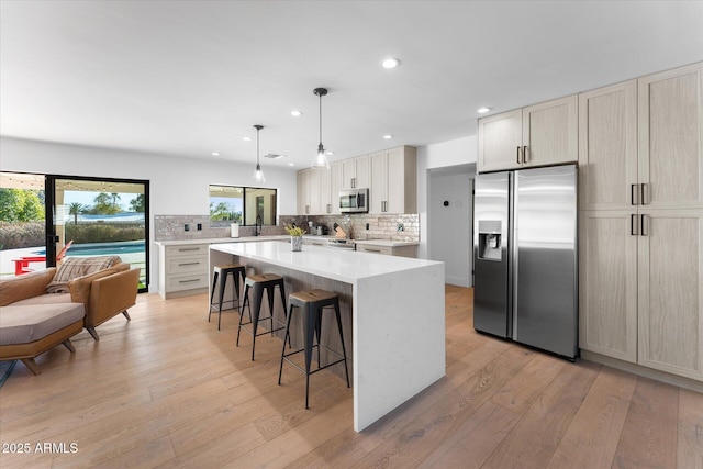 kitchen with appliances with stainless steel finishes, light hardwood / wood-style flooring, decorative backsplash, and hanging light fixtures