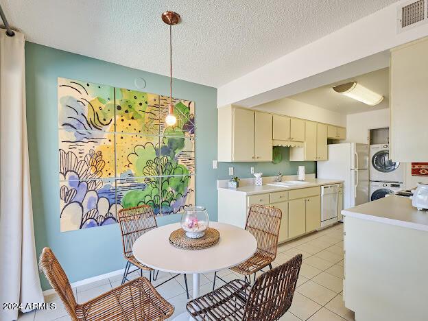 tiled dining space with sink, a textured ceiling, and stacked washer / drying machine