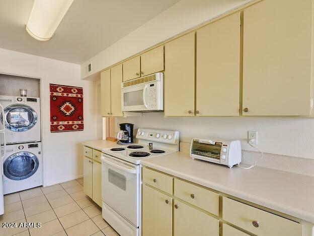 kitchen with stacked washing maching and dryer, white appliances, light tile patterned floors, and cream cabinets