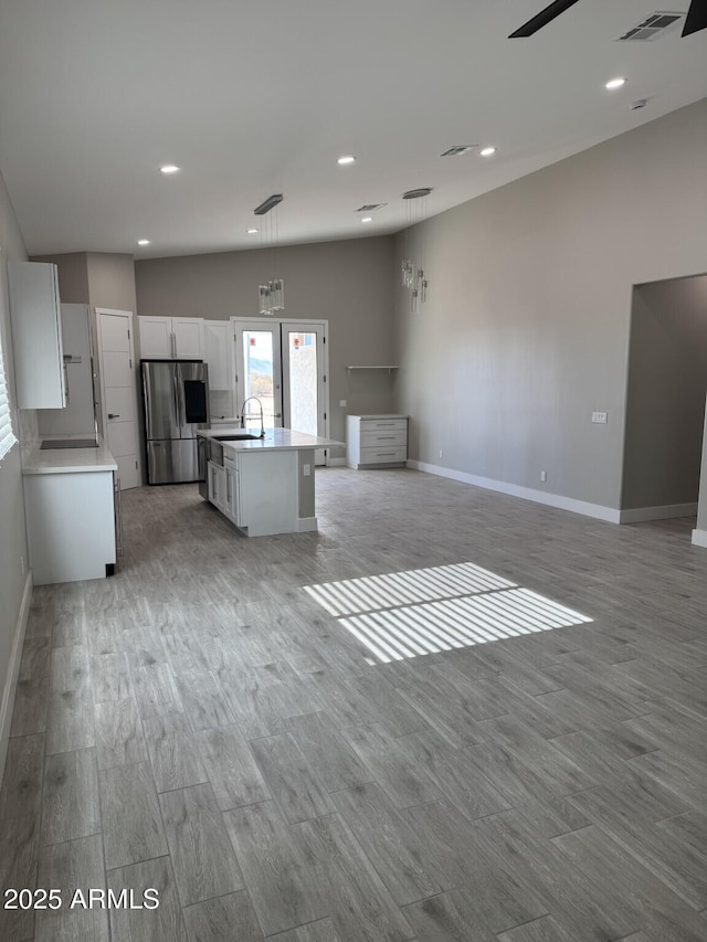 kitchen with decorative light fixtures, white cabinetry, an island with sink, stainless steel refrigerator, and light hardwood / wood-style flooring