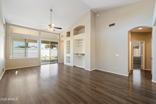 unfurnished room with arched walkways, built in shelves, a ceiling fan, and dark wood-style flooring