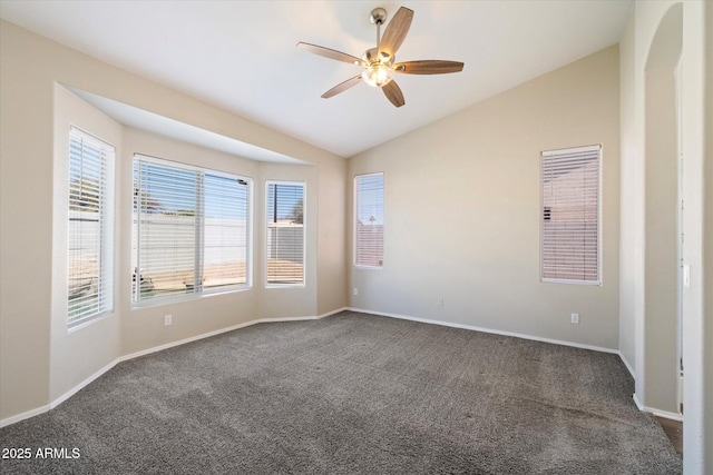 spare room with dark carpet, baseboards, ceiling fan, and vaulted ceiling