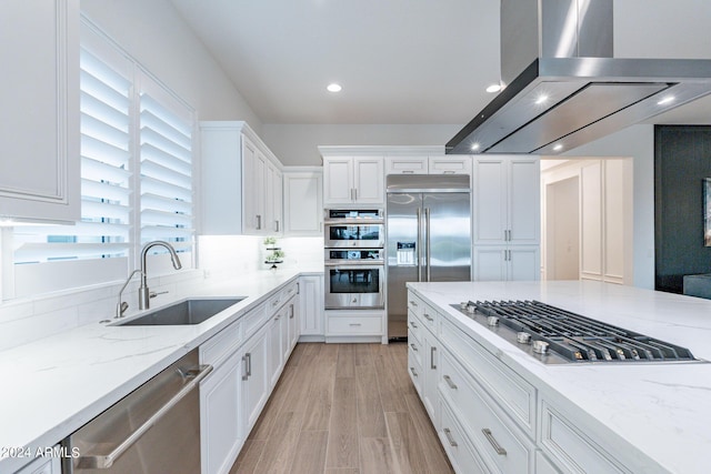 kitchen featuring sink, light stone counters, island range hood, stainless steel appliances, and white cabinets