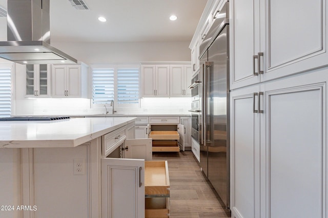 kitchen with white cabinets, island exhaust hood, black stovetop, and decorative backsplash