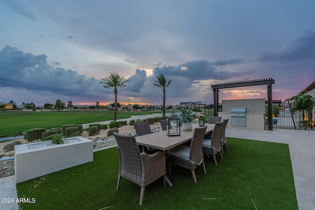 patio terrace at dusk featuring area for grilling, a lawn, and exterior kitchen