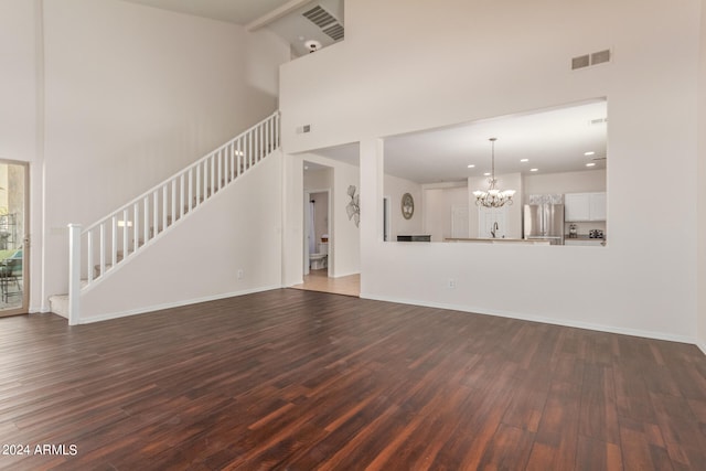 unfurnished living room featuring a towering ceiling, dark hardwood / wood-style flooring, a chandelier, and sink