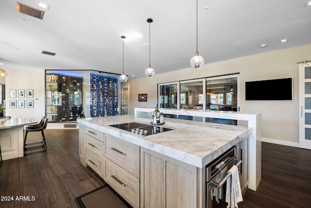 kitchen with light brown cabinetry, black electric cooktop, dark wood-type flooring, decorative light fixtures, and a center island with sink