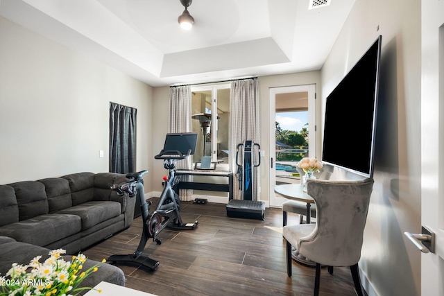 exercise room with a tray ceiling and dark wood-type flooring