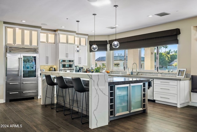 kitchen featuring hanging light fixtures, built in refrigerator, a kitchen island, dark hardwood / wood-style flooring, and white cabinetry