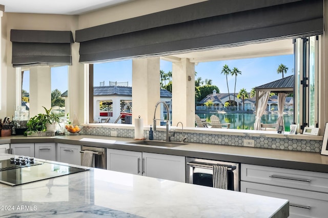 kitchen featuring decorative backsplash, black electric cooktop, sink, a water view, and white cabinets