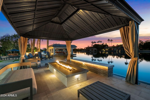 patio terrace at dusk featuring a gazebo, a water view, and an outdoor fire pit