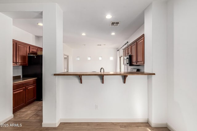 kitchen featuring light hardwood / wood-style floors, a kitchen breakfast bar, kitchen peninsula, and black fridge