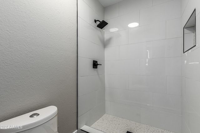 bathroom with toilet, a textured wall, and a tile shower