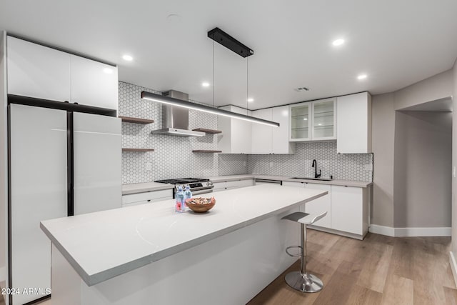 kitchen with light wood-style flooring, stainless steel gas stove, white cabinetry, wall chimney exhaust hood, and open shelves