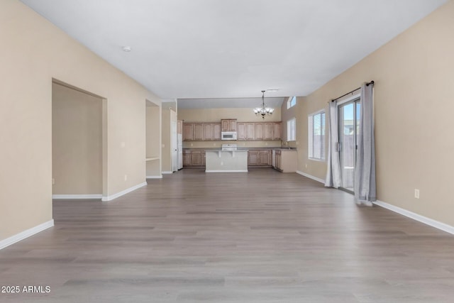 unfurnished living room with an inviting chandelier and light hardwood / wood-style flooring