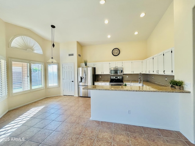 kitchen featuring light stone counters, appliances with stainless steel finishes, high vaulted ceiling, and a peninsula