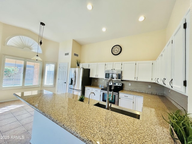 kitchen featuring light stone countertops, decorative backsplash, appliances with stainless steel finishes, a peninsula, and white cabinetry