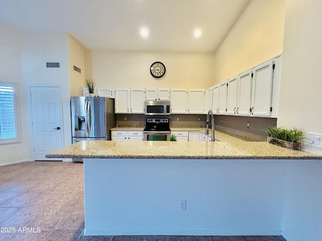 kitchen featuring visible vents, a peninsula, stainless steel appliances, and a high ceiling