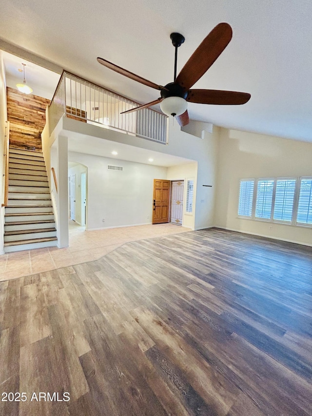 unfurnished living room with stairway, high vaulted ceiling, wood finished floors, and a ceiling fan