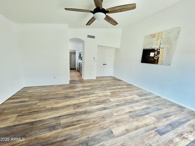 empty room with visible vents, ceiling fan, lofted ceiling, wood finished floors, and arched walkways