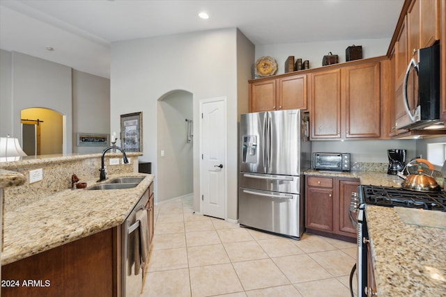 kitchen featuring a high ceiling, sink, light stone countertops, light tile patterned floors, and stainless steel appliances