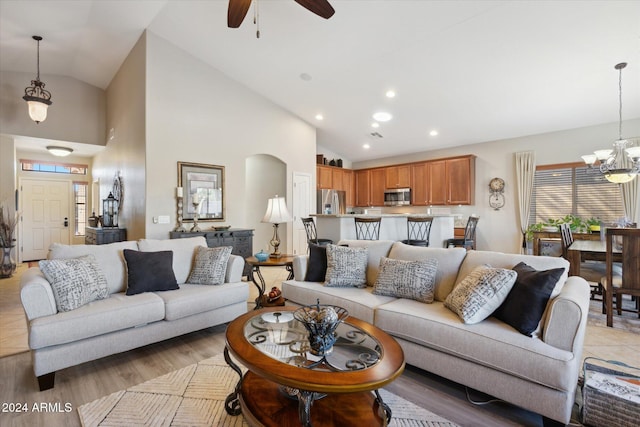 living room featuring ceiling fan with notable chandelier, light wood-type flooring, and high vaulted ceiling