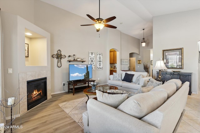 living room with ceiling fan, a fireplace, high vaulted ceiling, and light hardwood / wood-style floors