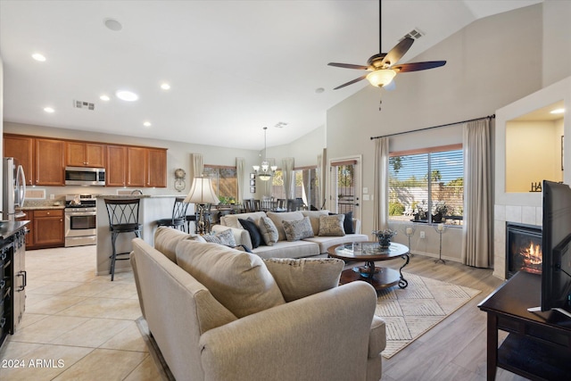 living room with ceiling fan with notable chandelier, lofted ceiling, and a tiled fireplace