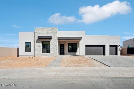 contemporary house with stone siding, stucco siding, an attached garage, and driveway