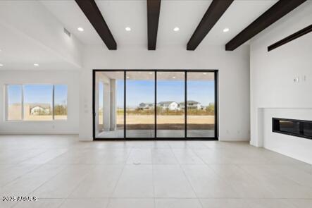 unfurnished living room featuring beam ceiling, plenty of natural light, and a glass covered fireplace