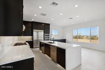 kitchen with visible vents, a kitchen island with sink, a sink, stainless steel appliances, and light countertops