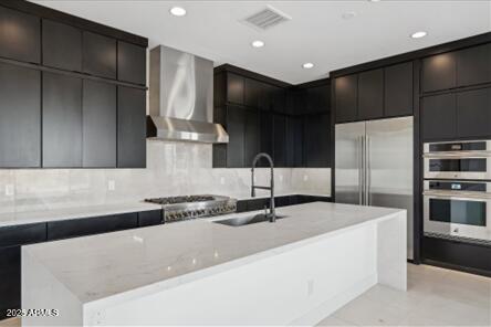 kitchen featuring visible vents, a sink, appliances with stainless steel finishes, wall chimney range hood, and modern cabinets