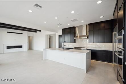 kitchen featuring visible vents, an island with sink, a barn door, modern cabinets, and wall chimney exhaust hood