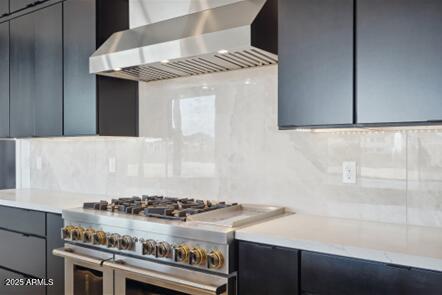 kitchen featuring modern cabinets, wall chimney range hood, backsplash, light countertops, and range with two ovens