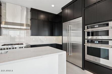 kitchen with modern cabinets, stainless steel appliances, wall chimney exhaust hood, and dark cabinets