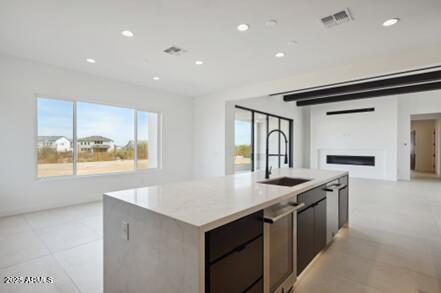 kitchen with visible vents, an island with sink, a sink, open floor plan, and light countertops