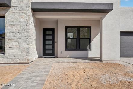 doorway to property with stucco siding, stone siding, and an attached garage